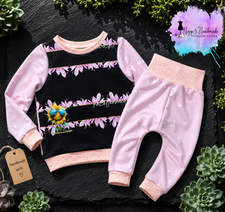 Handgenähtes Kinder-Outfit für Handmade-Liebhaber: Ein rosa-schwarzer Pullover mit Sonnenblumen-Motiv und eine passende rosa Pumphose, dekoriert mit Sukkulenten und einem Niggi's Handmade Logo.