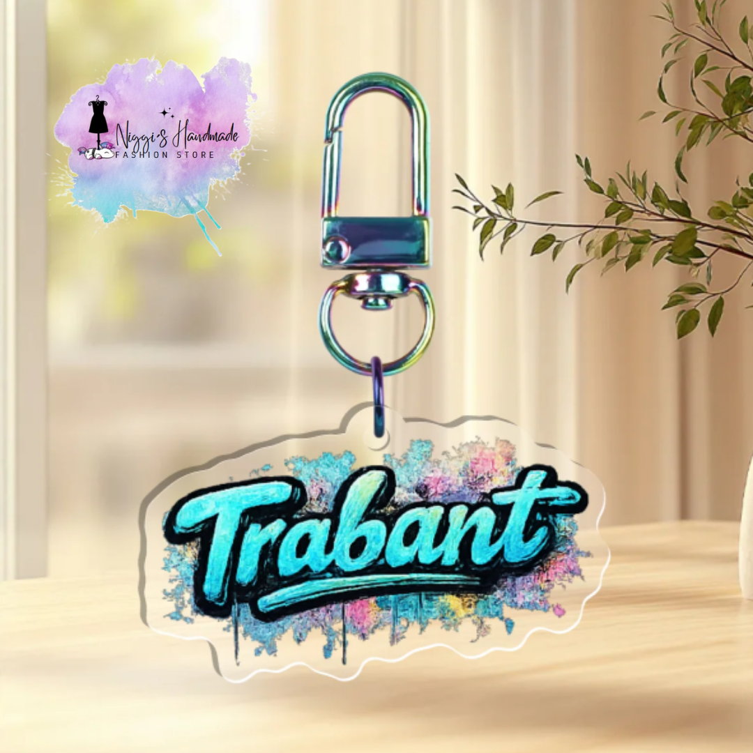 Transparenter Schlüsselanhänger aus Acryl mit dem blau-weißen Graffiti-Schriftzug „Trabant“ auf einer bunten Sprühfarbe-Optik, befestigt an einem bunt schimmernden Karabinerhaken.