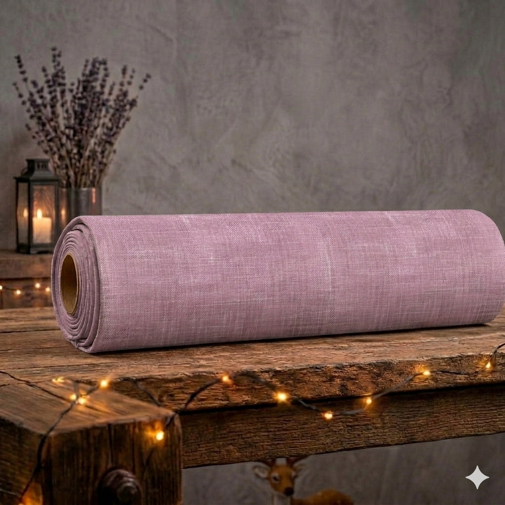 Eine aufgerollte Stoffrolle des altrosafarbenen French Terry Allover-Stoffs „Zarte Struktur“ von Niggi's Handmade liegt auf einem rustikalen Holztisch. Das Design zeigt eine melierte Textur im Denim- und Leinen-Look. Im gemütlichen Hintergrund stehen getrockneter Lavendel und eine Laterne mit brennender Kerze, umrahmt von einer warm leuchtenden Lichterkette im Vordergrund. Unter dem Tisch schaut der Kopf einer kleinen Rehkitz-Figur hervor.