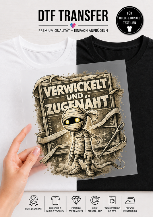 Ein transparentes DTF-Transfer-Bügelbild, gehalten von einer Hand vor einem geteilten T-Shirt-Hintergrund (links weiß, rechts schwarz). Das Motiv zeigt eine kleine Comic-Mumie mit Bandagen und leuchtend gelben Augen. Um die Mumie herum schweben eine Nähnadel und ein Faden. Im Hintergrund ist eine alte, rissige Steintafel mit dem deutschen Schriftzug „VERWICKELT UND ZUGENÄHT“ im Vintage-Stil zu sehen. Am oberen und unteren Rand sind Produktinfos auf Deutsch platziert.