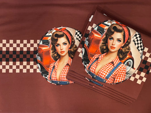 Produktbild des exklusiven French-Terry-Panelstoffes „Vintage Pin-Up Hot Rod“ von Niggi's Handmade Fashion Store. Auf einem kastanienbraunen Stoffhintergrund ist das runde Motiv einer Pin-Up-Frau im 50er-Jahre-Stil mit rot-weiß kariertem Hemd vor einem orangefarbenen Hot-Rod-Oldtimer und einer Zielflagge abgebildet. Rechts daneben liegt ein Stapel desselben gefalteten Stoffes. Ein horizontales, braun-beiges Schachbrettmuster zieht sich über den Stoff.