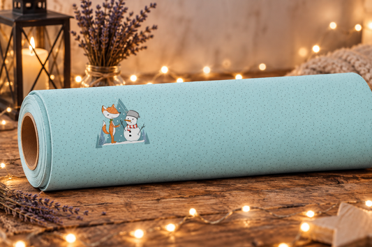 Eine hellblaue Stoffrolle des French Terry Panels „Beste Winterfreunde“ liegt auf einer rustikalen Holzoberfläche. Das Stoffdesign zeigt ein feines Pünktchenmuster und ein zentrales Motiv mit einem kleinen Comic-Fuchs und einem Schneemann vor gezeichneten Tannenbäumen. Dekoriert ist die Szene mit einer leuchtenden Lichterkette, getrocknetem Lavendel und einer brennenden Kerze in einer Laterne.